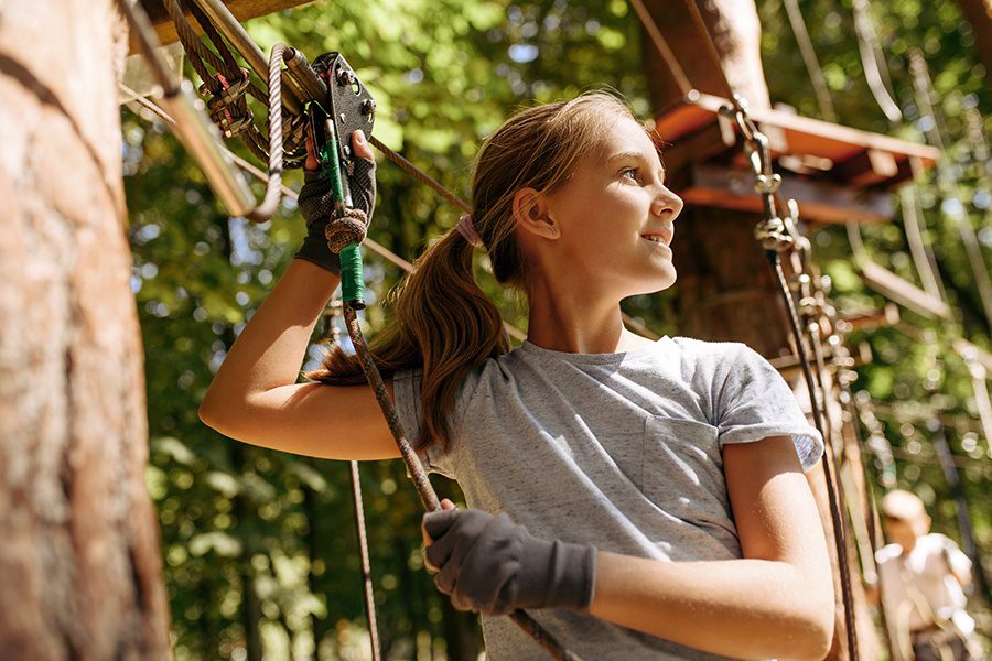 Adventure and Entertainment Insurance - Closeup of Young Girl Climbing Rope and Tree While Using a Harness at an Aerial Adventure Park
