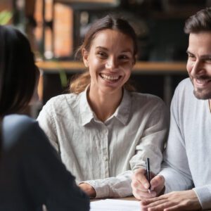 An image of a happy couple signing a document across the table from a woman in professional attire