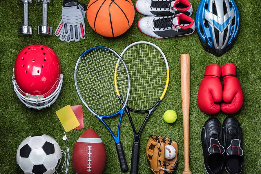 Sport Equipment Insurance - Sporting Equipment Like Helmets, Sports Balls, Gloves, Rackets, and a Bat on a Green Grass Floor