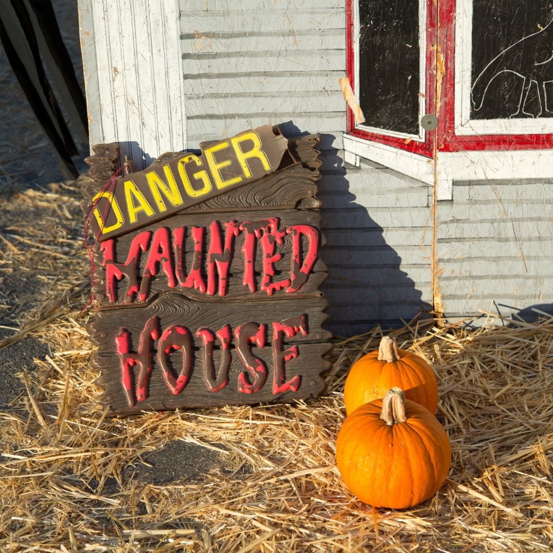 Haunted house sign with pumpkins on some hay