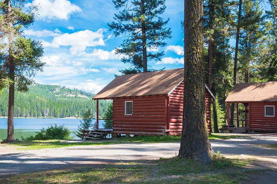 Campground Insurance - Rustic Tiny Log Homes Facing the Lake with Mountain Views on a Campground on a Sunny Day